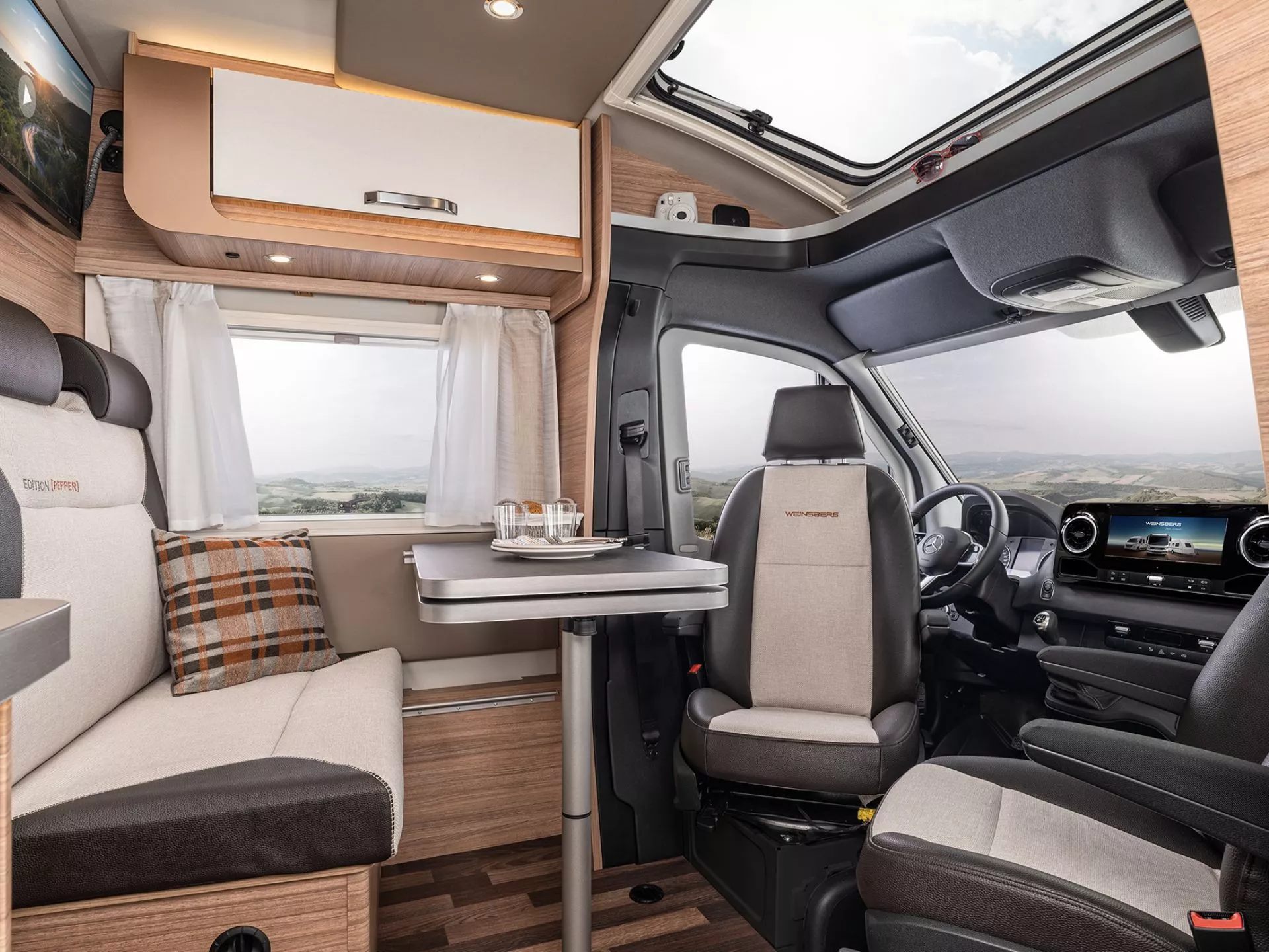Der Innenraum eines Wohnmobils zur Sitzecke mit Tisch und den umgedrehten Fahrersitzen im Fahrerhaus