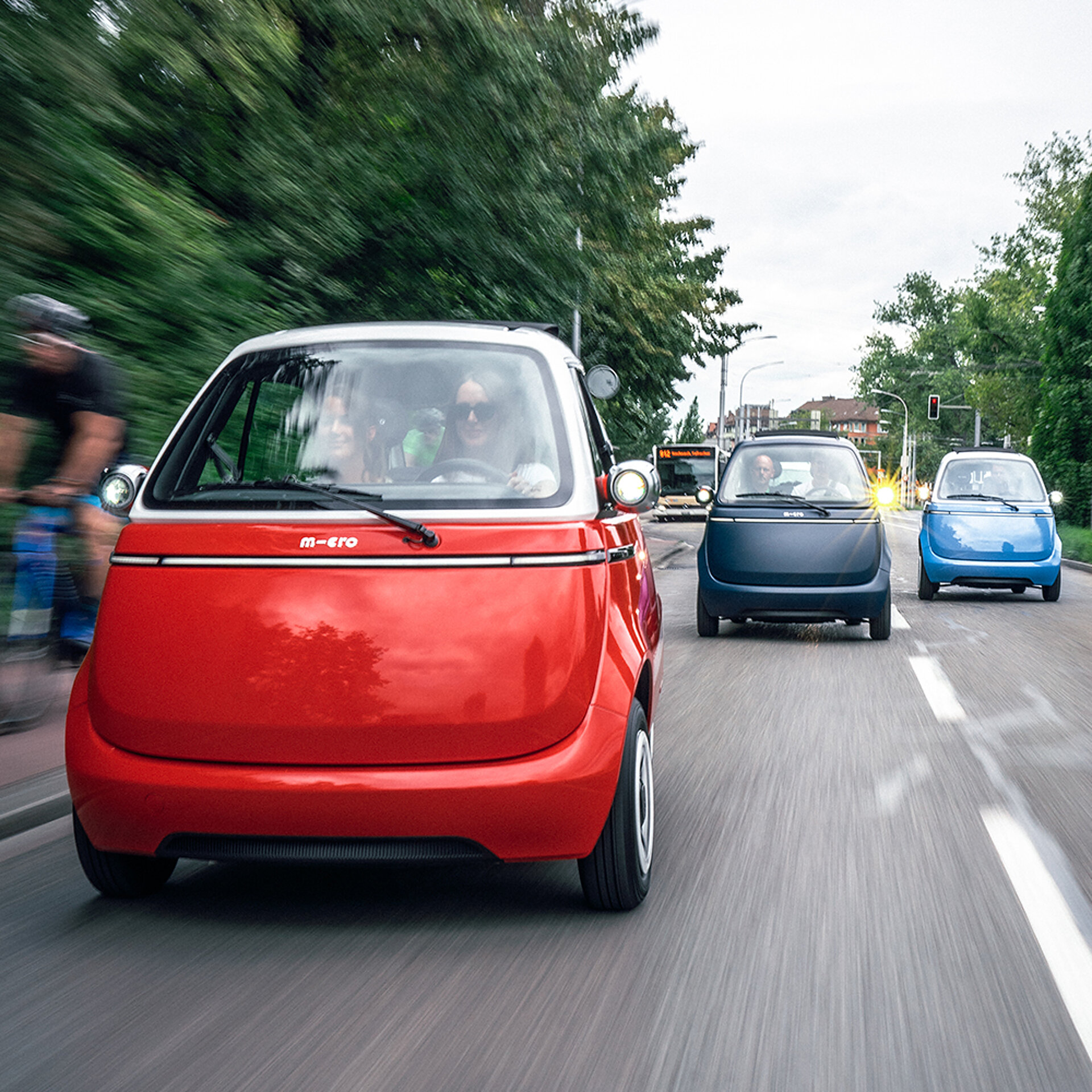 Mehrere Microlino Micro Cars fahren eine Straße entlang.