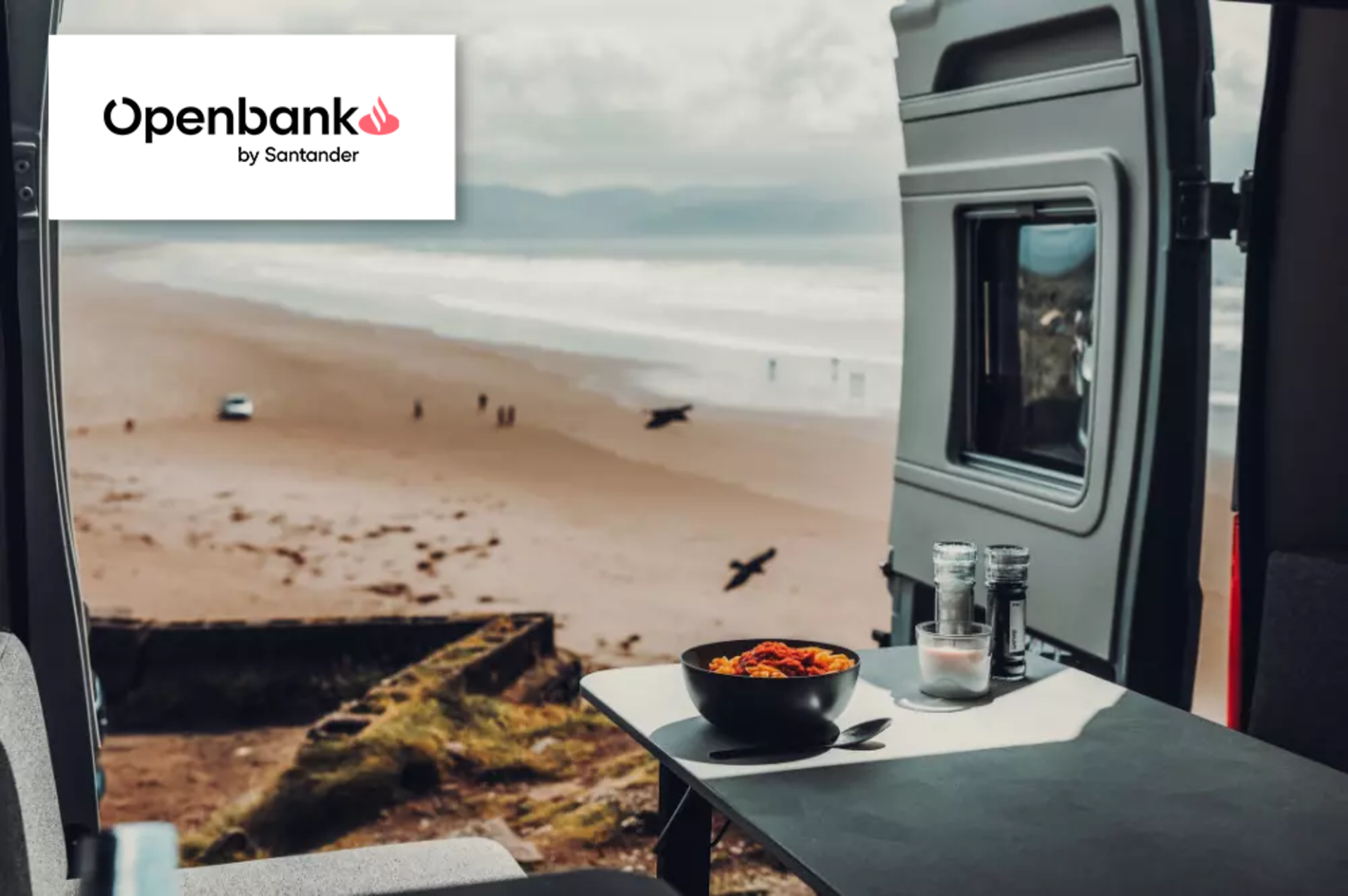 Blick aus dem Heck eines Camper Vans auf einen Strand, gebrandet mit Santander Logo.