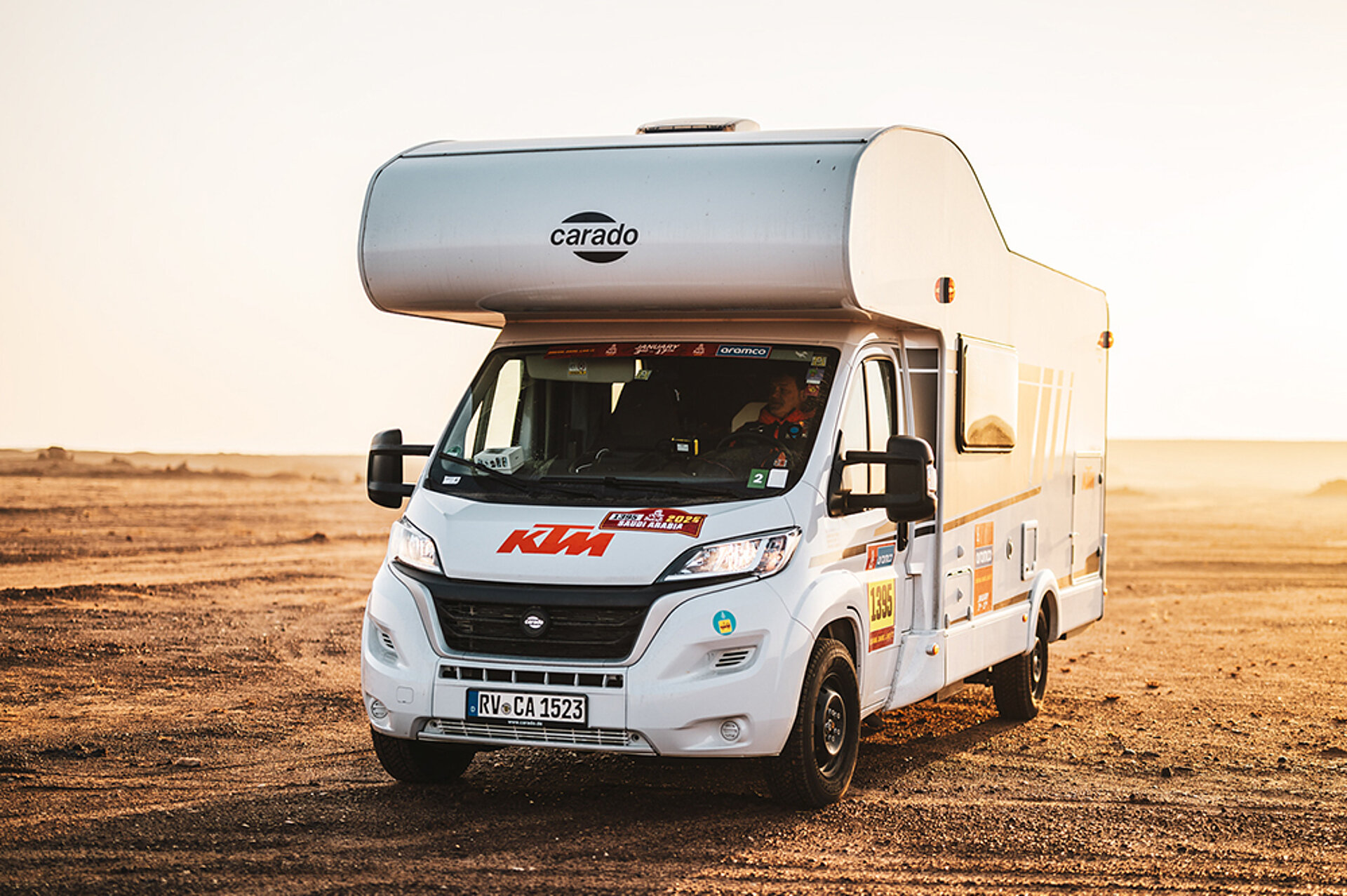 Ein Miet-Wohnmobil mit Alkoven steht im Gegenlicht in einer Steppe.