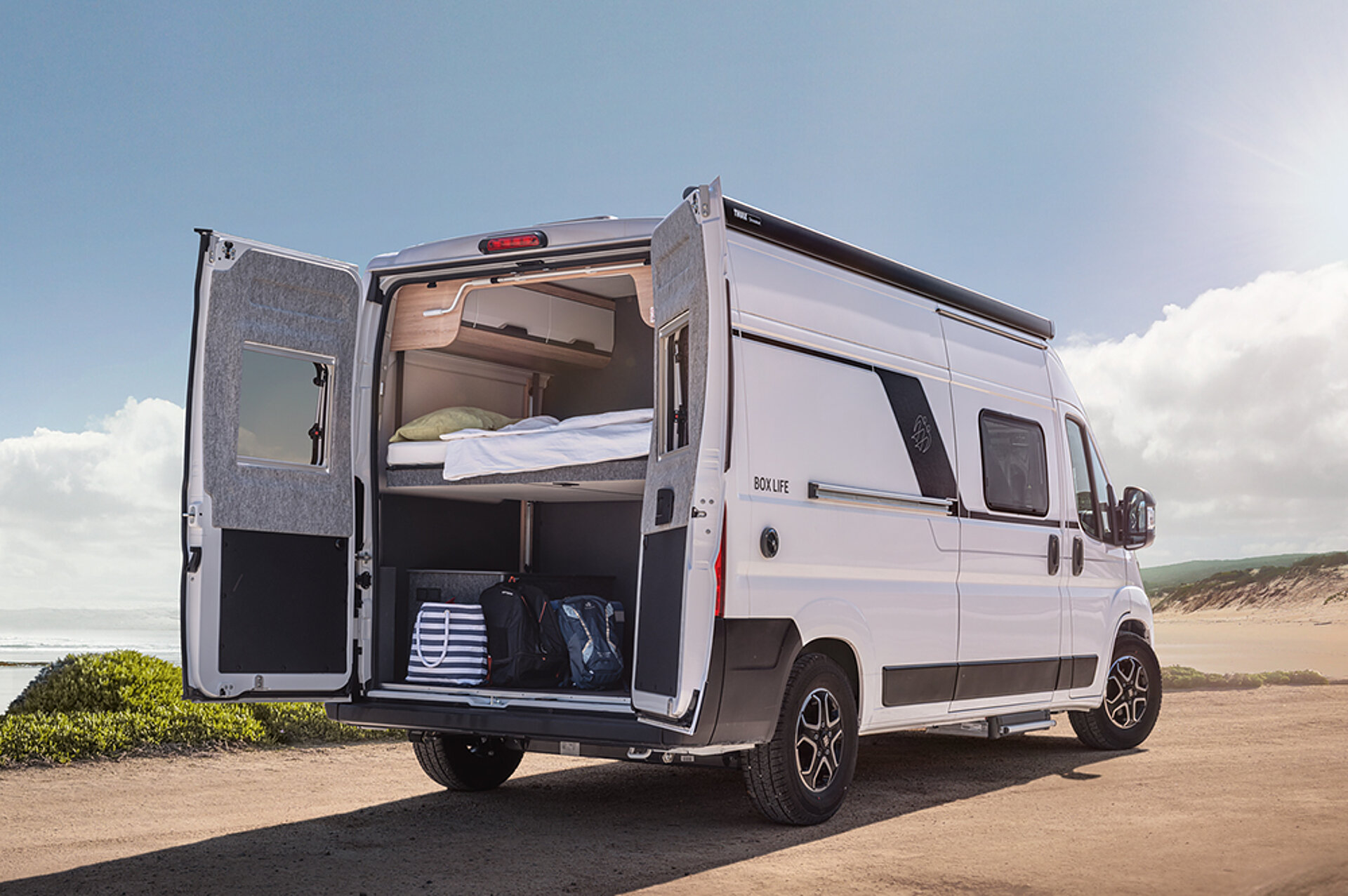 Karavan KNAUS z řady PLATINUM SELECTION stojí s otevřenou zadní částí v pouštní krajině.