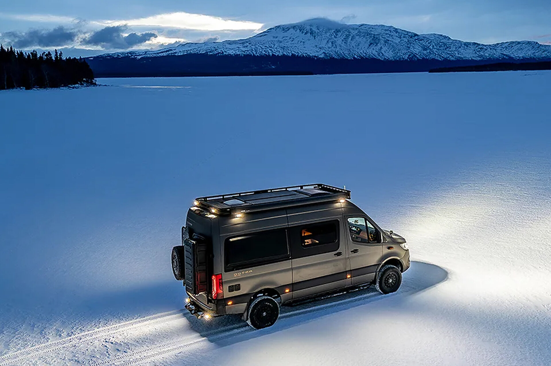 Ein Dovra Camper Van steht mit angeschaltetem Licht bei Nacht inmitten einer großen Schneewüste.