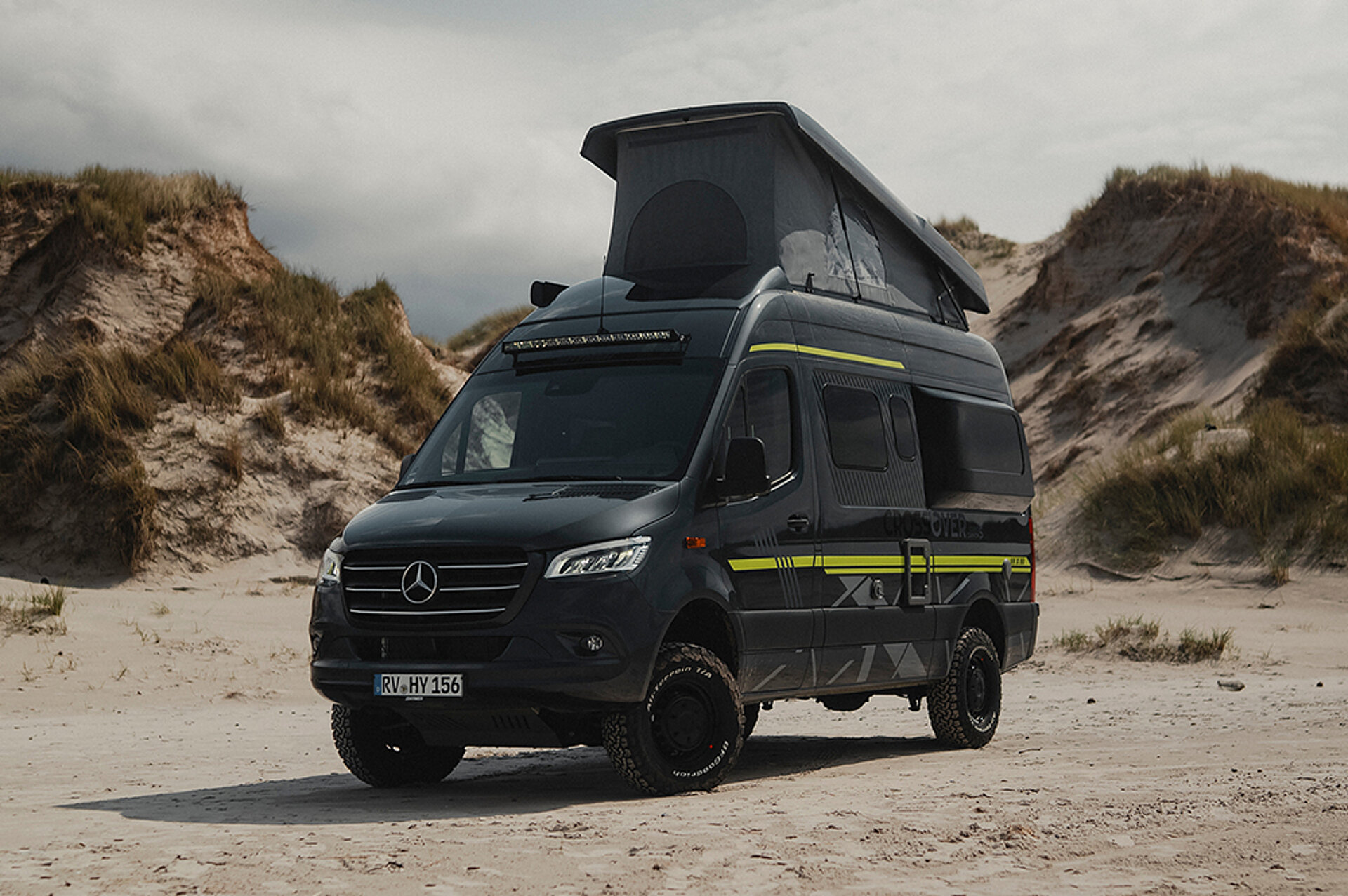Ein HYMER Camper Van mit aufgestelltem Hubdach parkt an einem Strand.