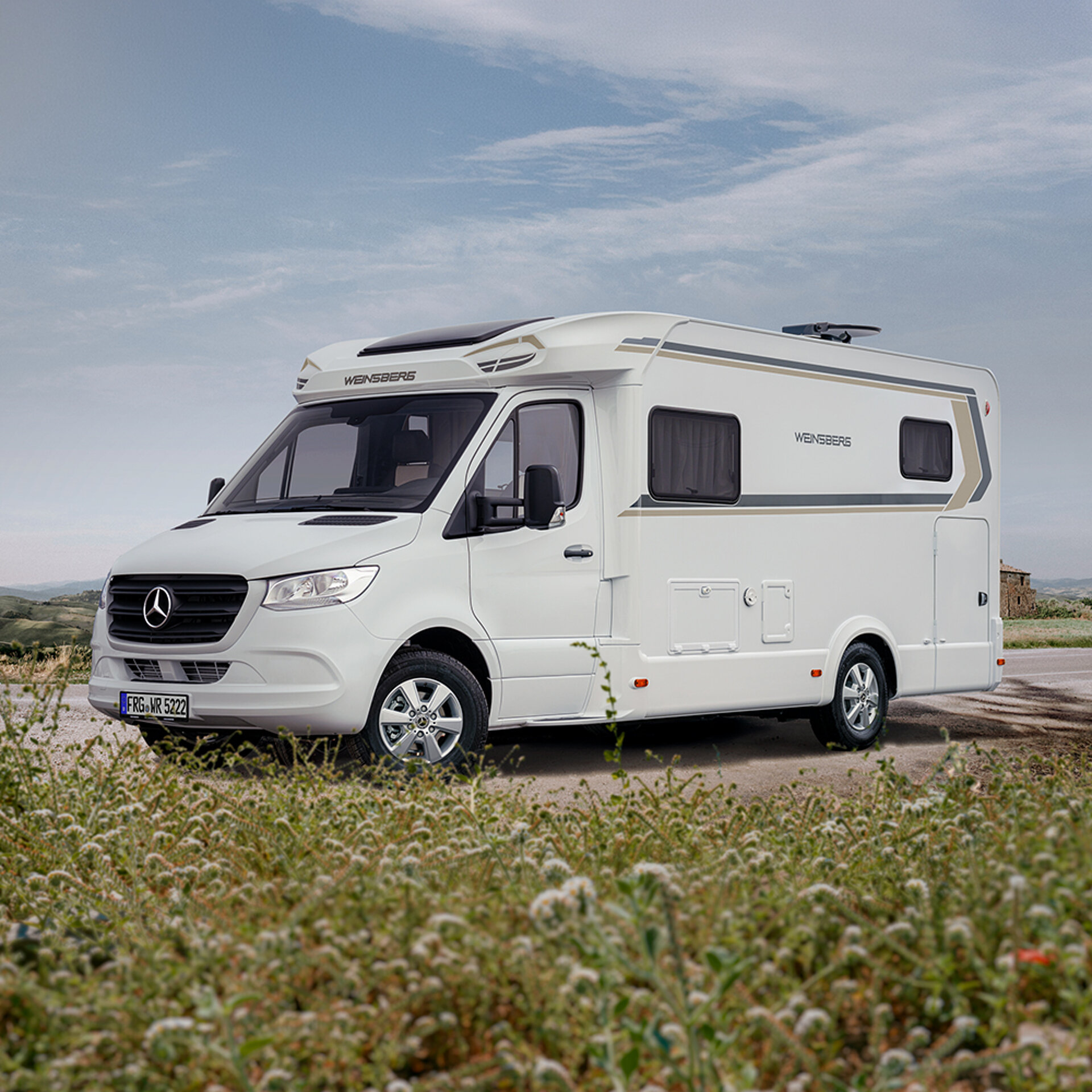 Ein WEINSBERG Reisemobil parkt auf einer Straße neben einem Wald.
