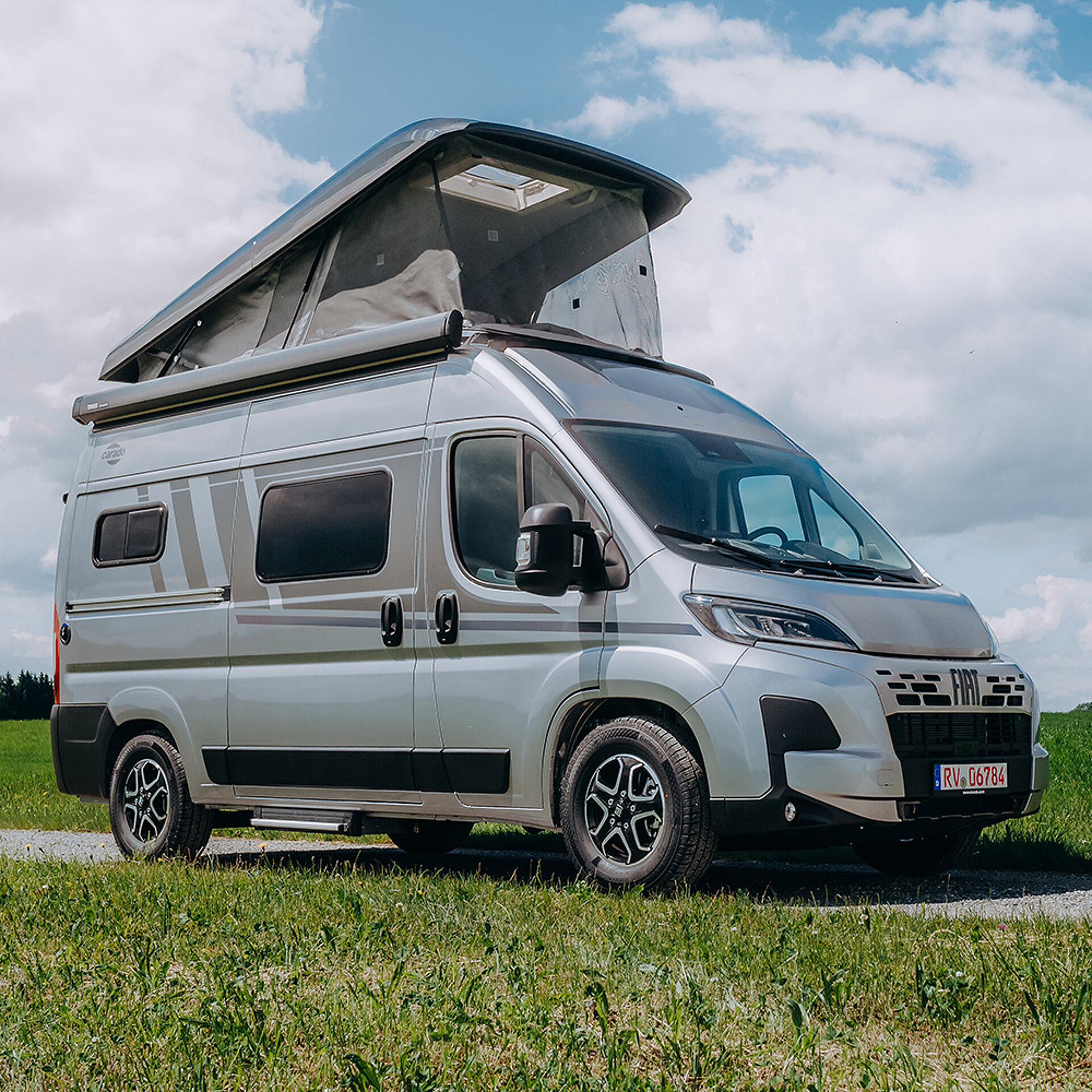 Karavan s výklopnou střechou parkuje na silnici, která vede přes louku.