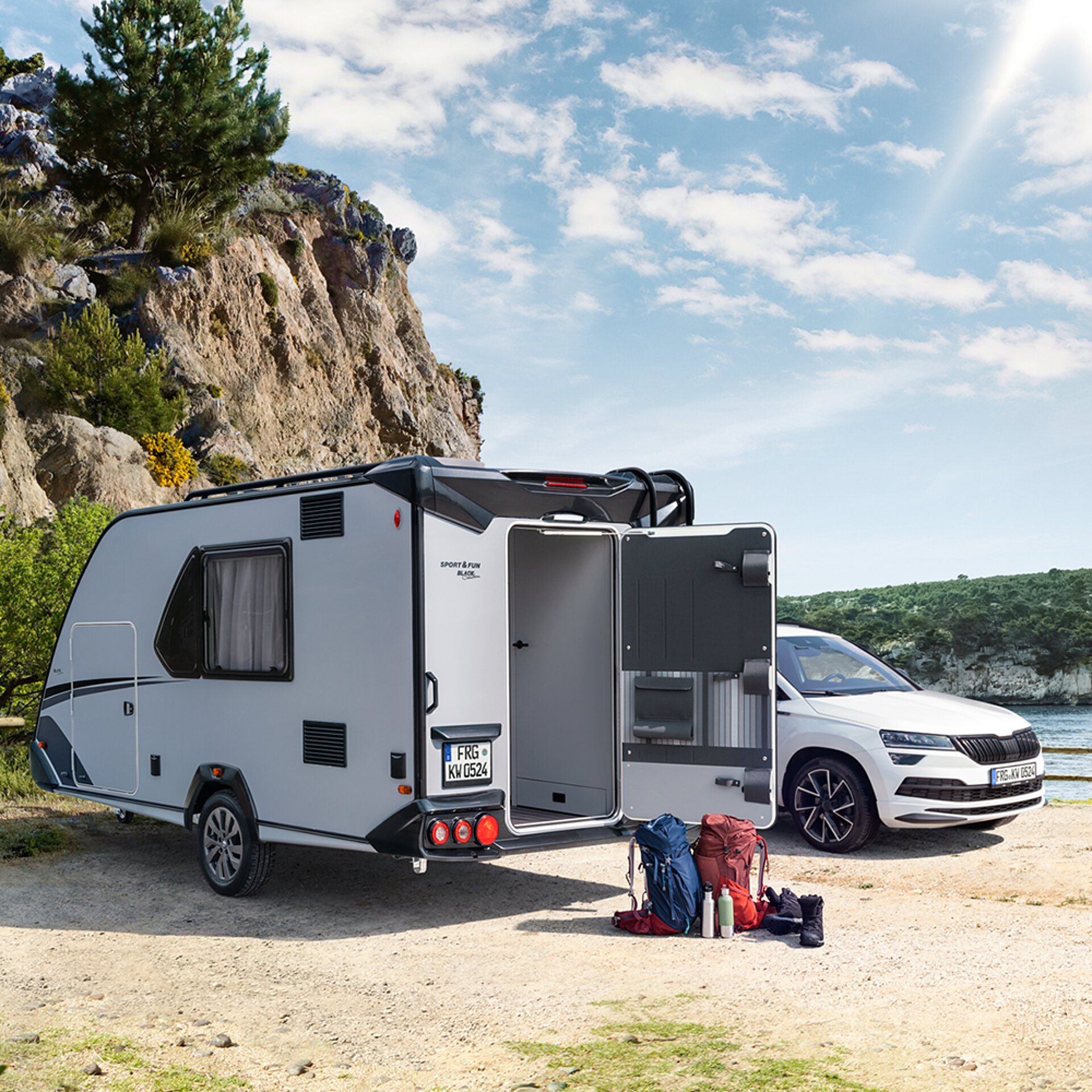 A small KNAUS caravan is parked next to a car by a lake.