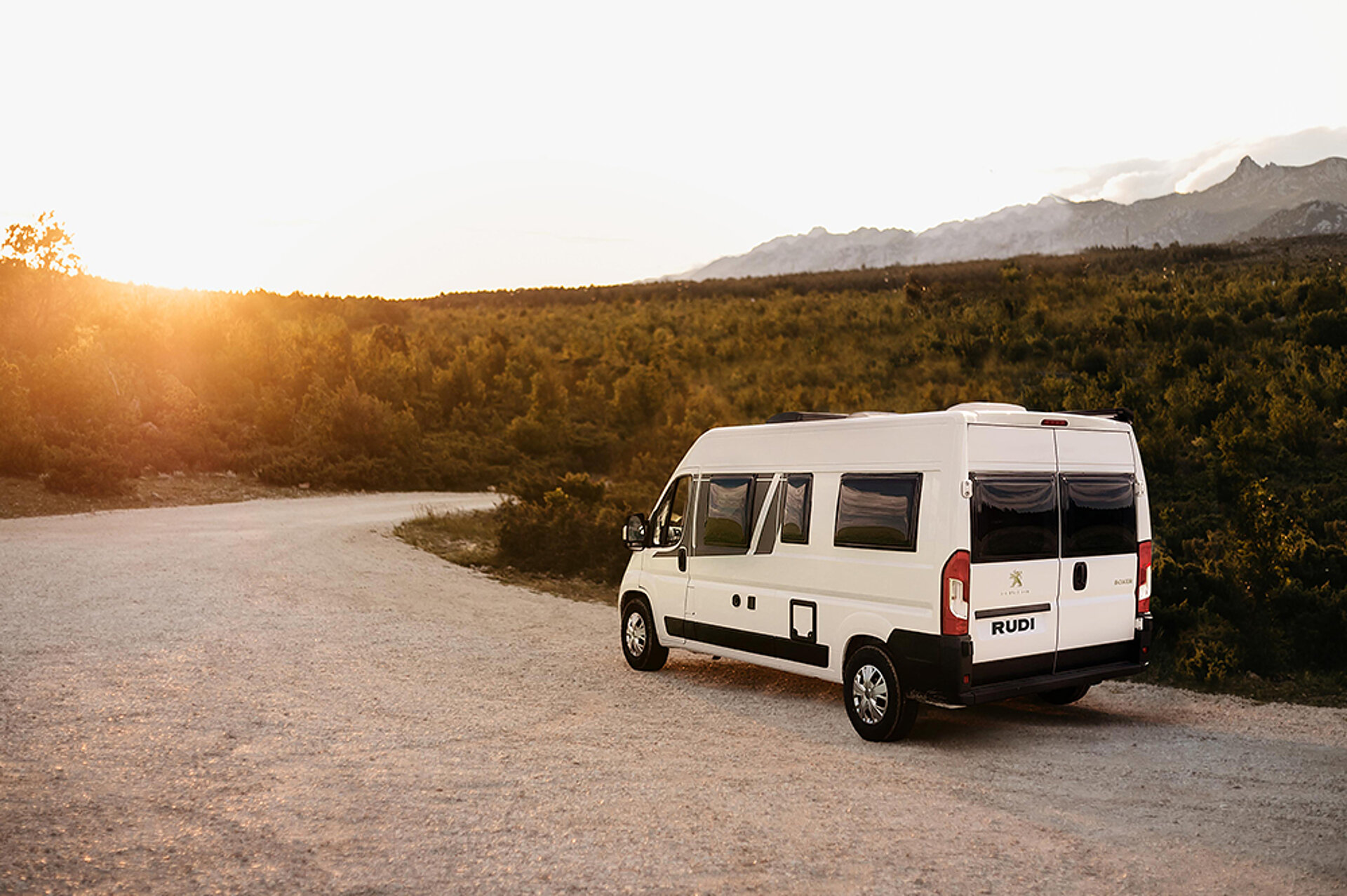 Heckansicht vom Carado CV640 Kastenwagen, der auf einer Landstraße in den Sonnenuntergang fährt.