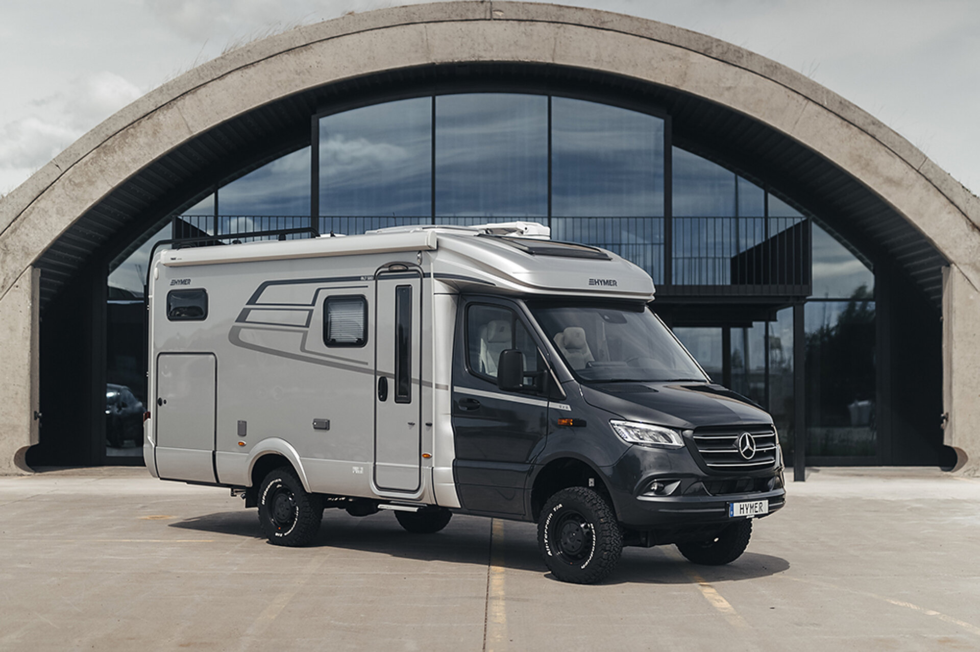 Der HYMER ML-T – eine Stilikone. Ein HYMER ML-T 580 steht vor der Glasfront eines runden Gebäudes.