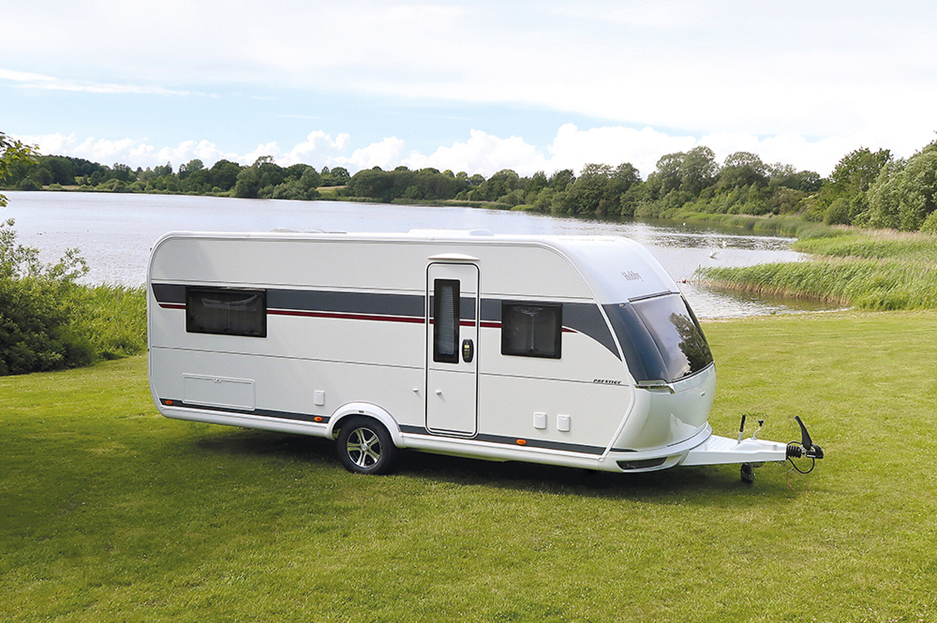 Ein Hobby PRESTIGE Caravan geparkt auf einer Wiese vor einem Waldsee.