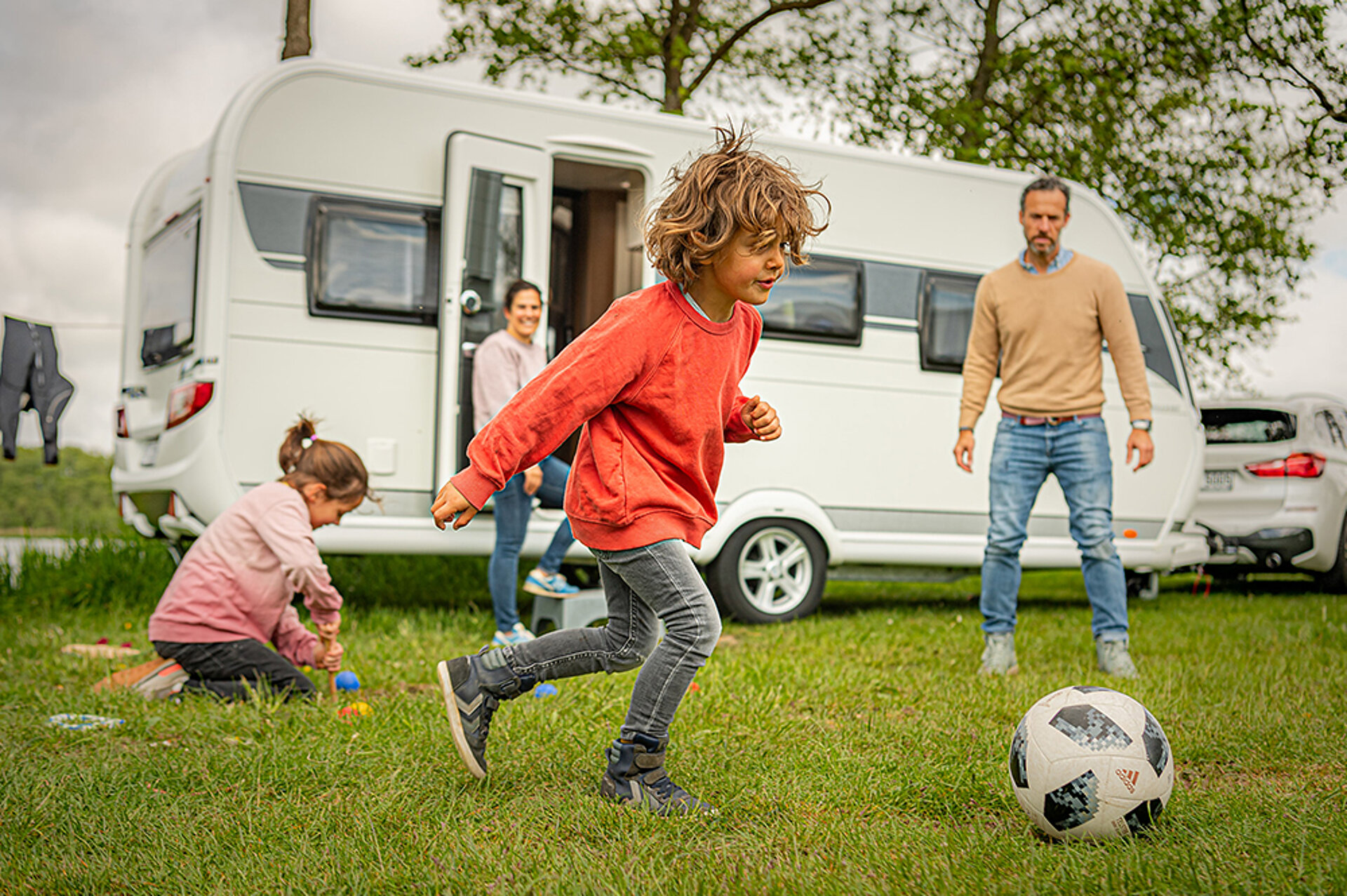 Bei schaffer-mobil machen wir Ihren Urlaubstraum war. Eine Familie spielt auf einer Wiese vor einem Wohnwagen Fußball.