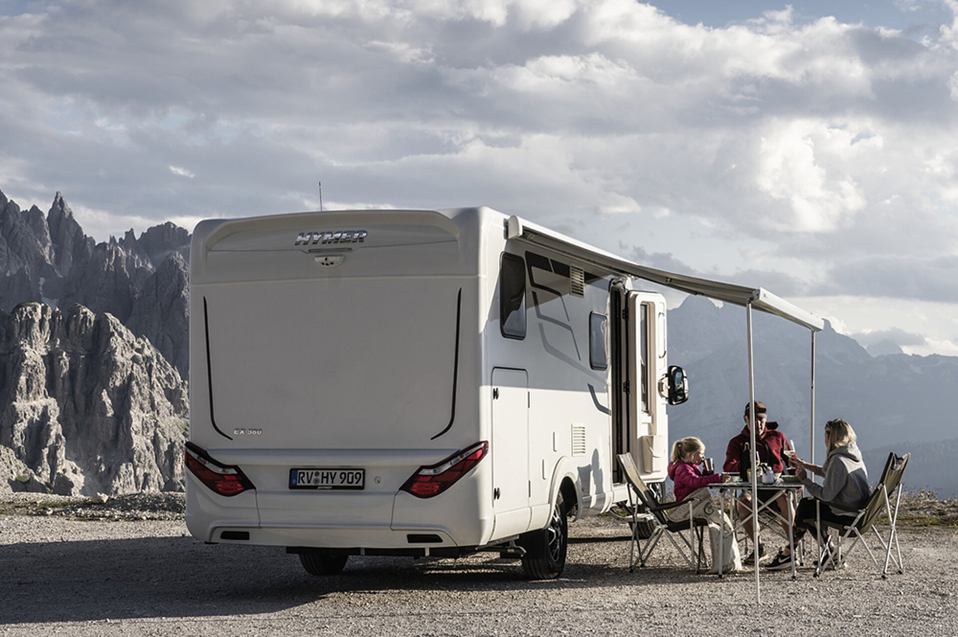Mit einem eigenen Wohnmobil vereinen Sie Freiheit, Komfort und Naturnähe. Eine Familie sitzt am Campingtisch unter der Markise ihres Wohnmobils