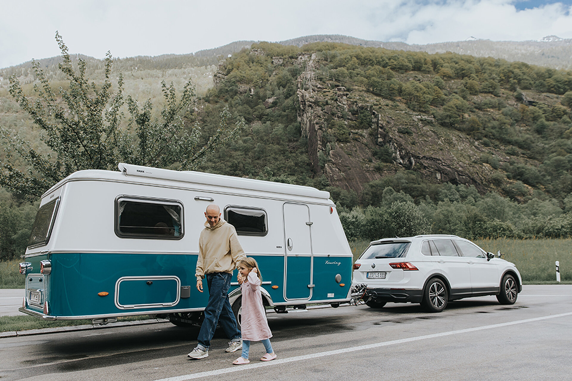 Dank geringer Kosten kann sich jeder den Traum vom gebrauchten Caravan erfüllen. Ein Vater läuft mit seiner Tochter an einem Wohnwagen vorbei, der am Straßenrand geparkt steht.