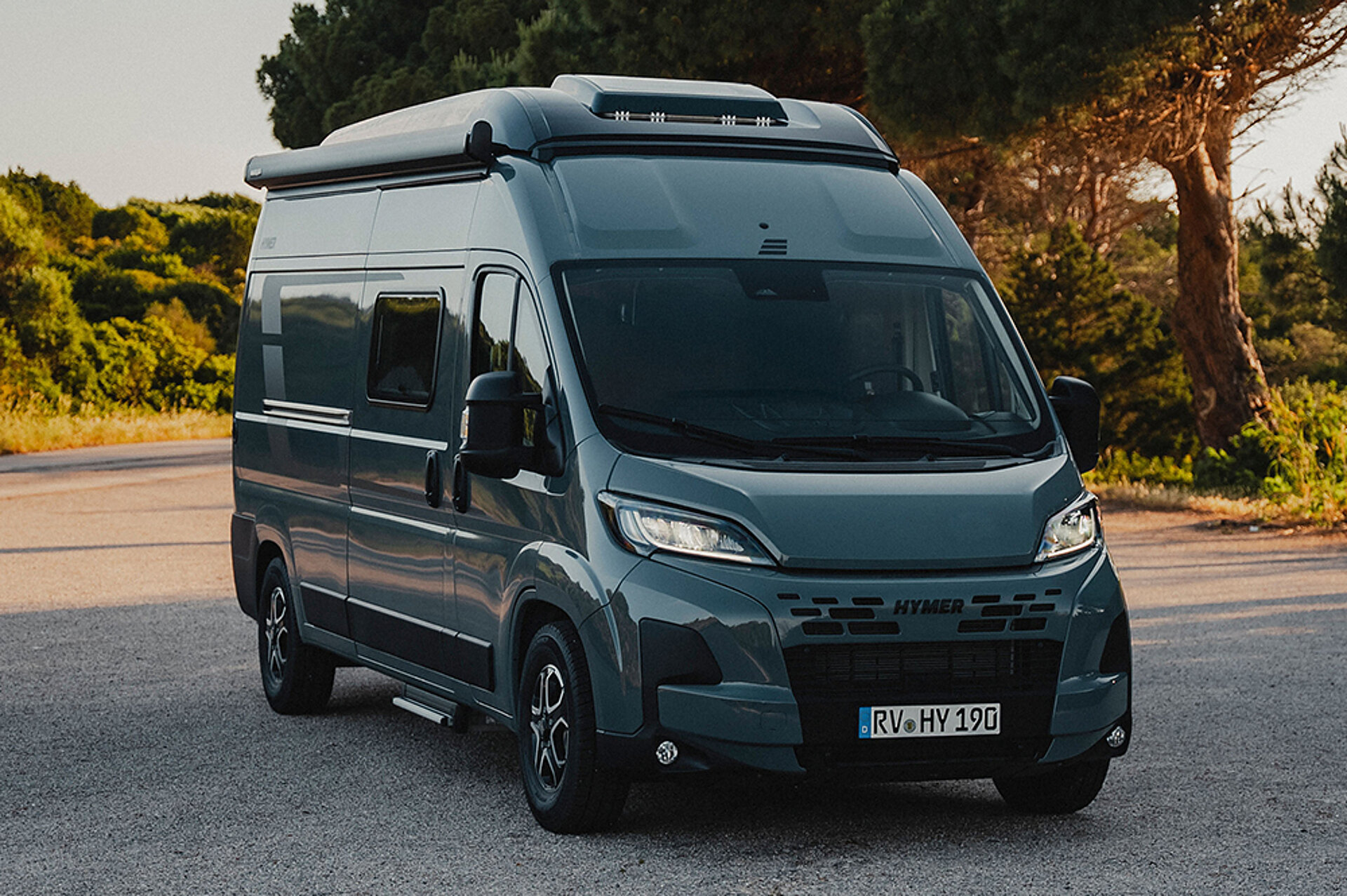 Ein HYMER Kastenwagen parkt vor einem Wald im Sonnenuntergang.