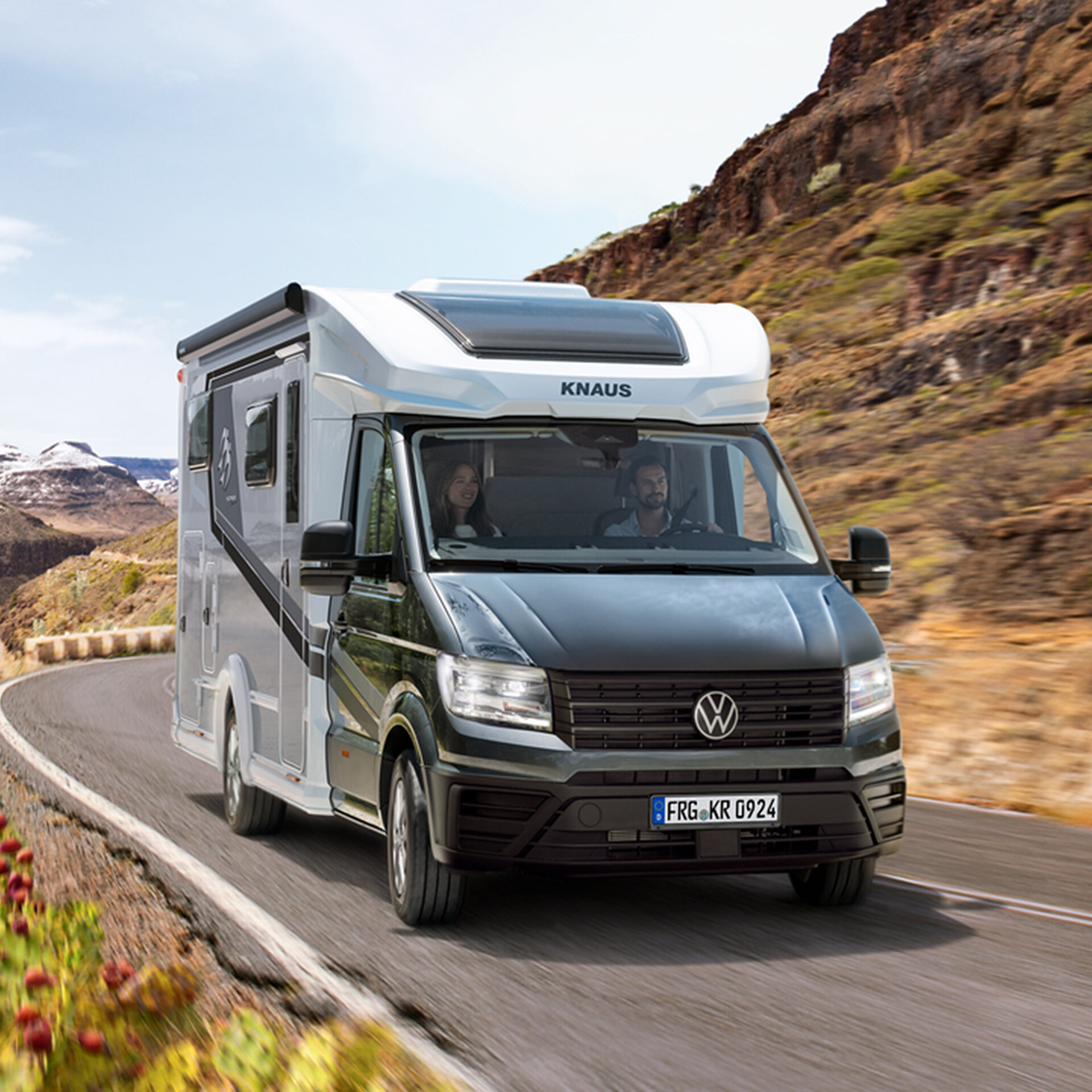 A KNAUS motorhome is driving along a road through a mountainous landscape.