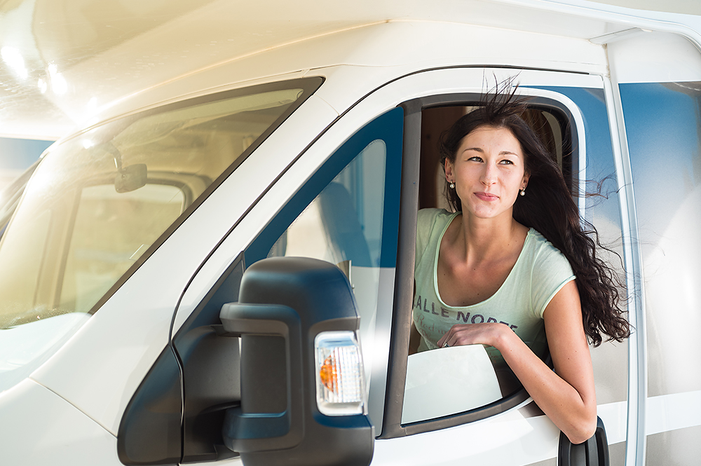 Eine junge Frau schaut aus dem Fahrerfenster eines Wohnmobils.