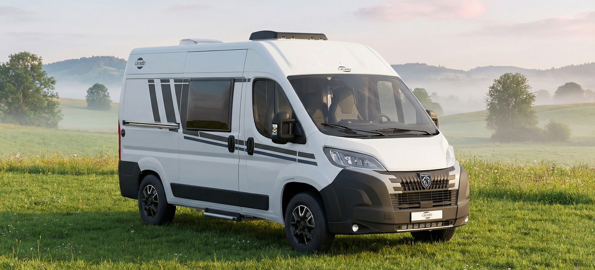 Pohled zepředu na obytný vůz Carado CV540, který stojí na zelené louce v lehké ranní mlze.