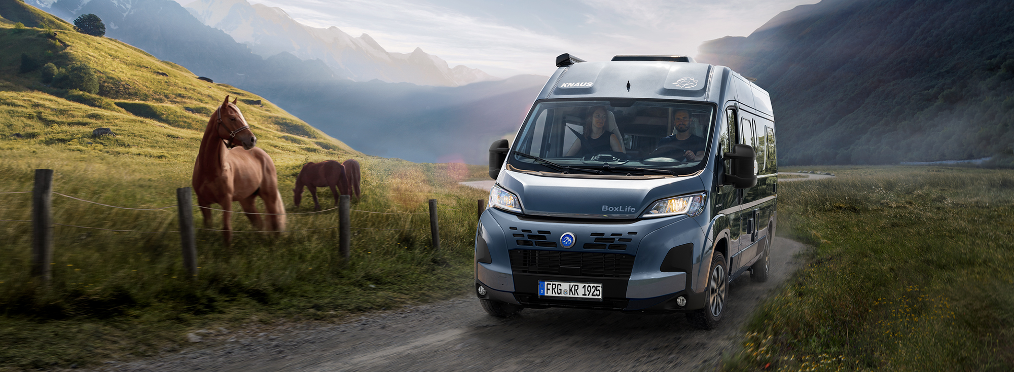 Ein KNAUS BOXLIFE Camper Van fährt auf eine Landstraße neben einer Pferdewiese entlang.