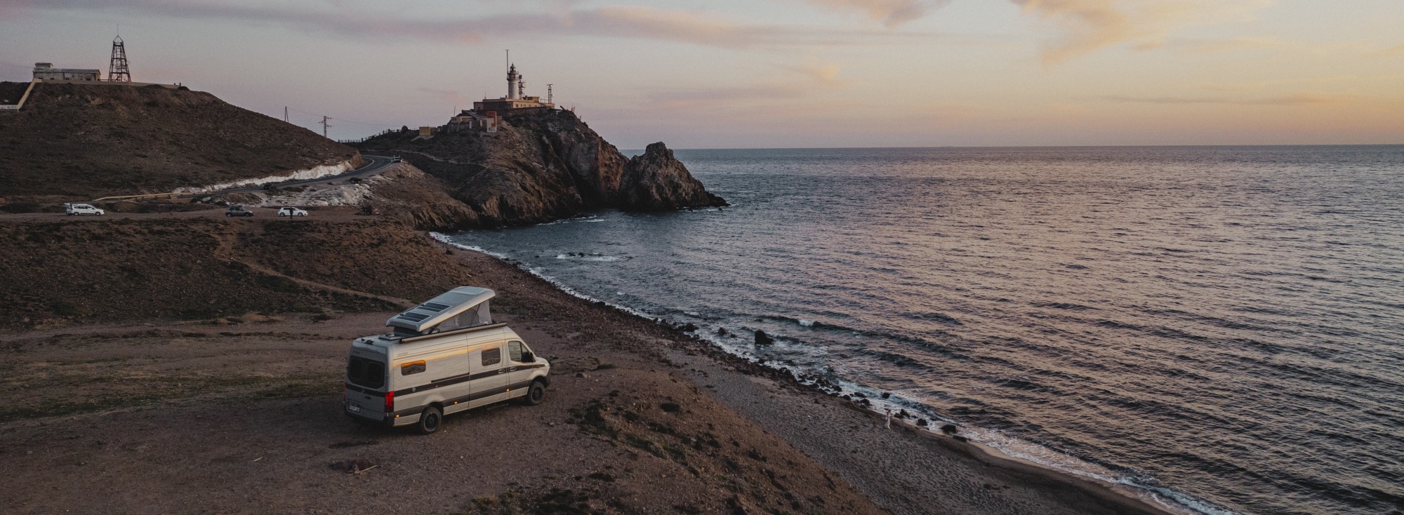 Ein Camper Van parkt an einem Meer in Sonnenuntergang.