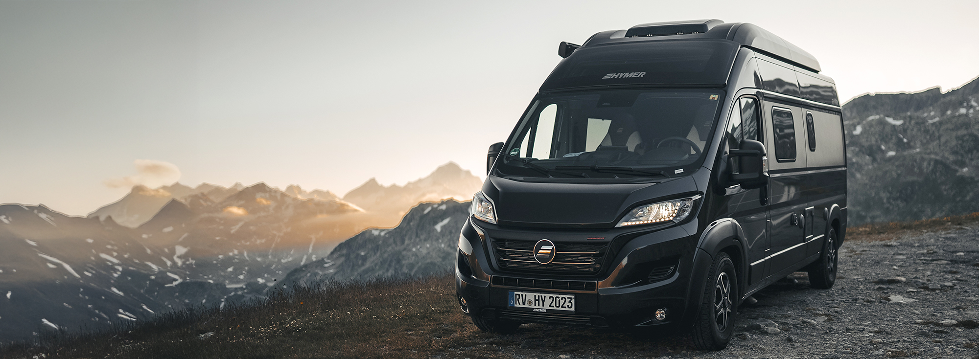 Ein Camper Van parkt neben einer Bergstraße.