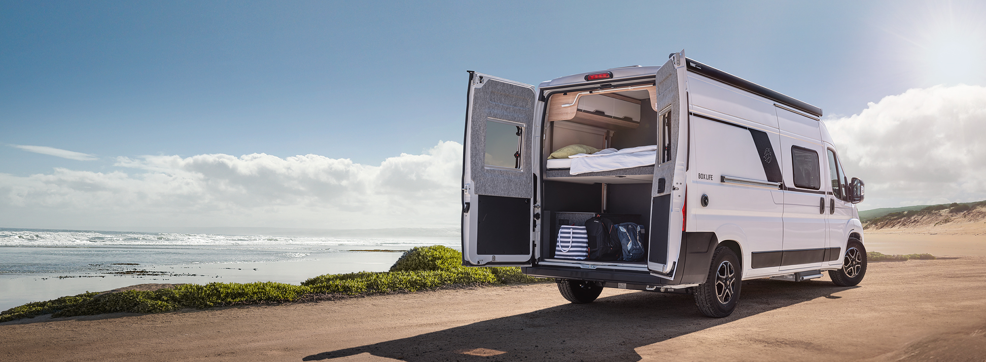 Obytný vůz KNAUS řady PLATINUM SELECTION stojí s otevřenou zadní částí v pouštní krajině.