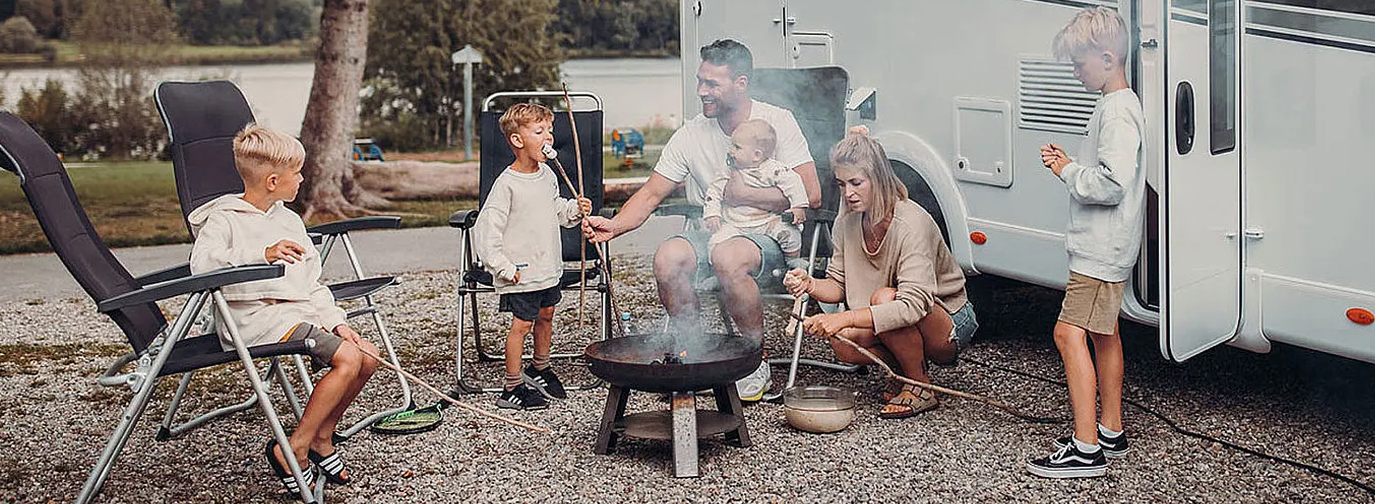 Eine Familie sitzt an einer Feuerschale vor einem gemieteten Wohnmobil.