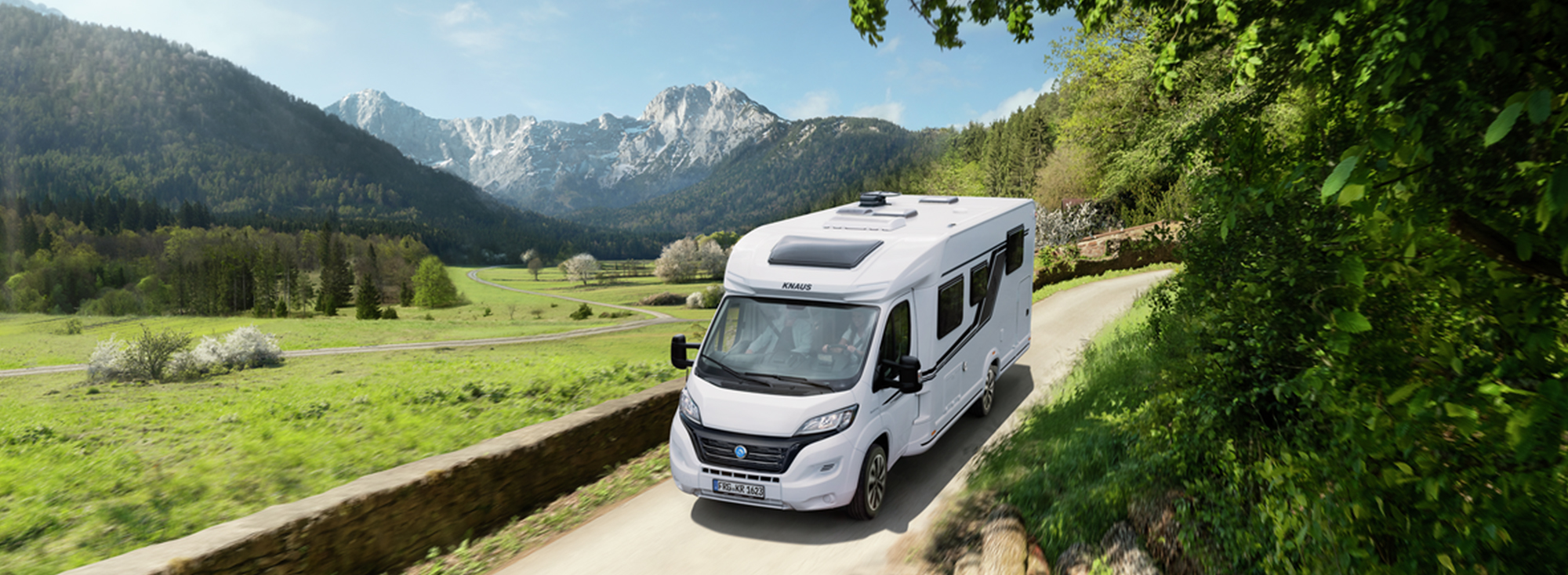 Ein neues Wohnmobil fährt einen kleinen Weg neben einer grünen Wiese entlang.