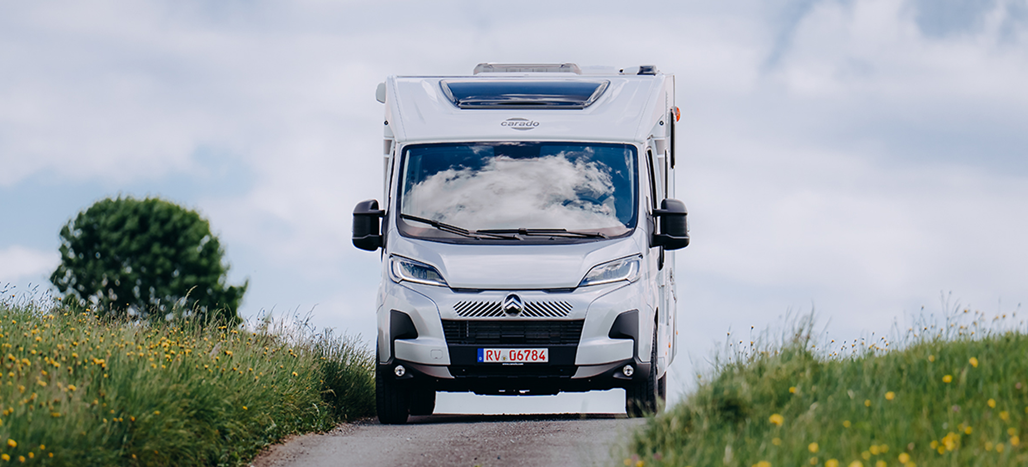 Carado V347 projíždí loukou po úzké silnici.