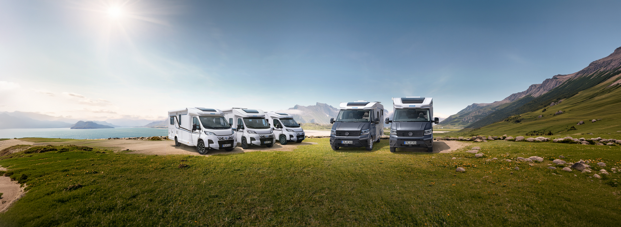 Alle teilintegrierten Reisemobile von KNAUS stehen auf einer Wiese nebeneinander. 