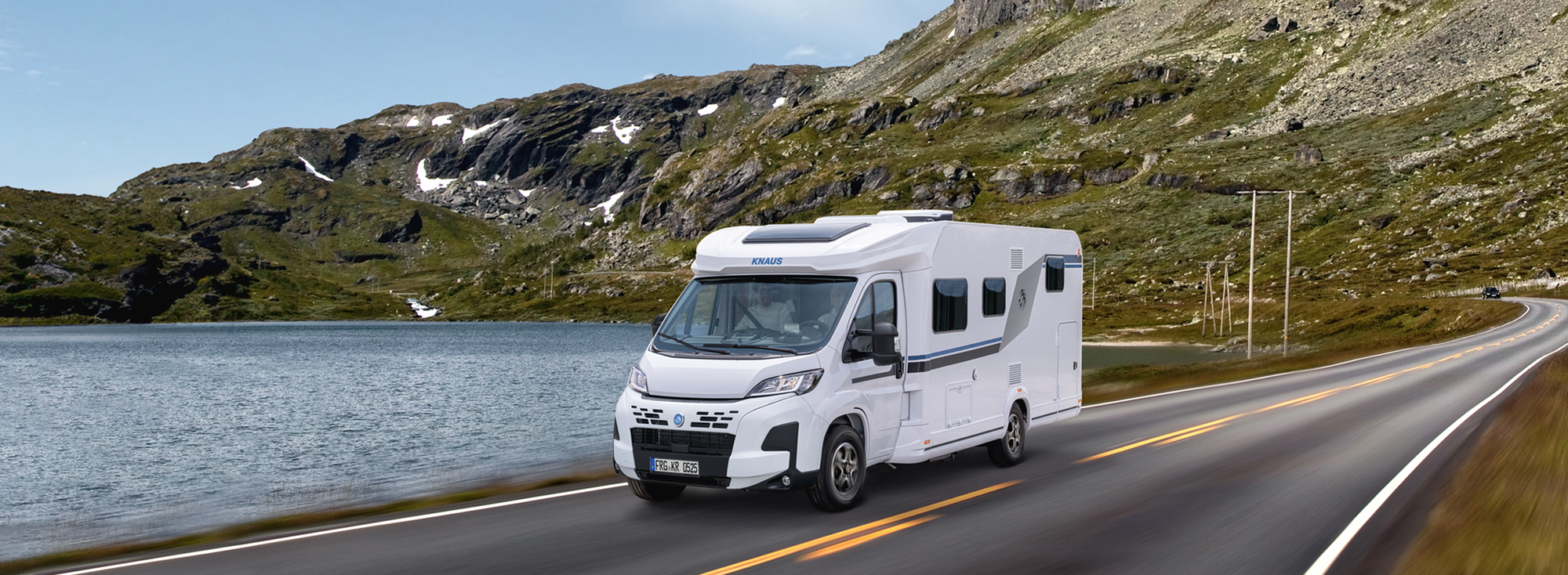 Ein KNAUS L!VE TI fährt eine Straße neben einem See entlang.