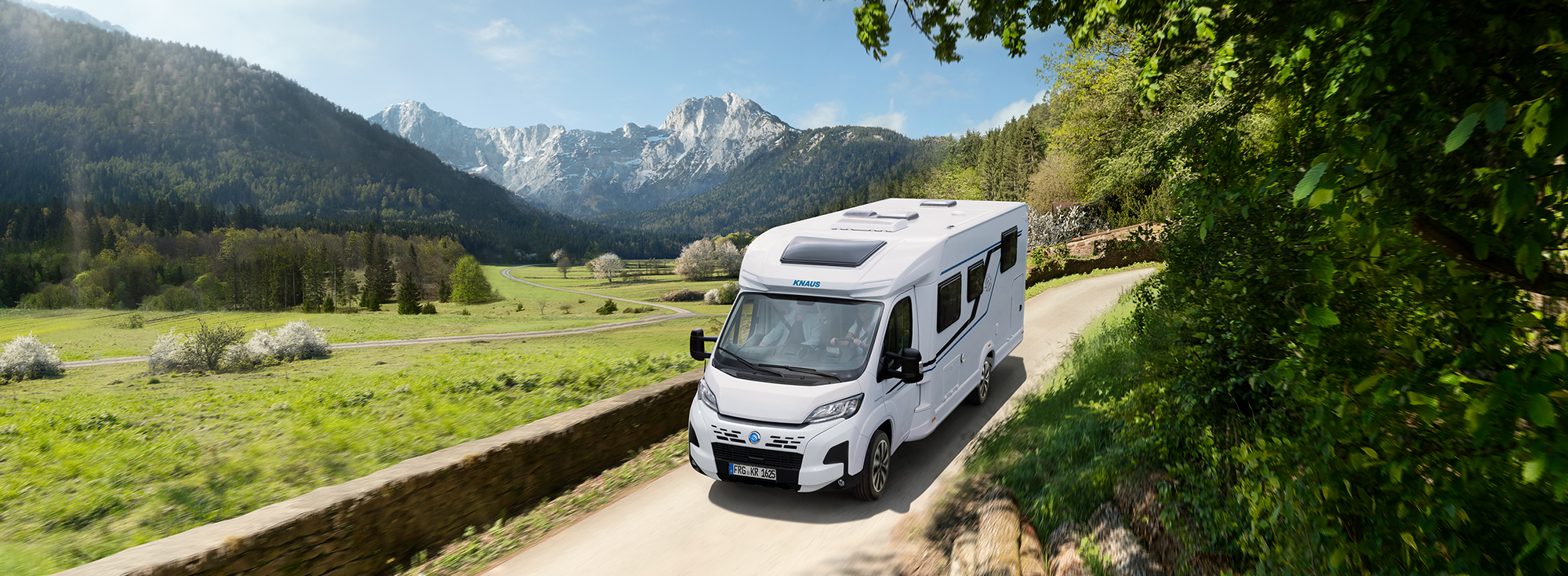 Ein KNAUS SKY TI fährt eine Straße durchs Grüne entlang.