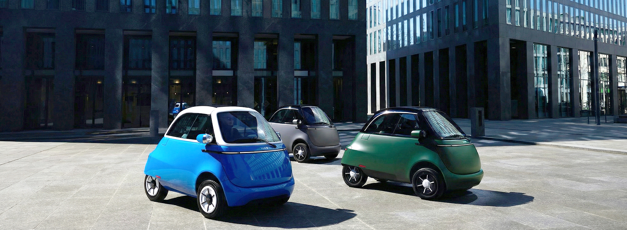 Drei Microlino Micro Cars parken auf einem Platz in der Stadt.