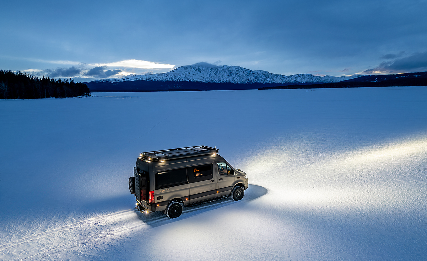 Ein Dovra Camper Van steht mit angeschaltetem Licht bei Nacht inmitten einer großen Schneewüste.